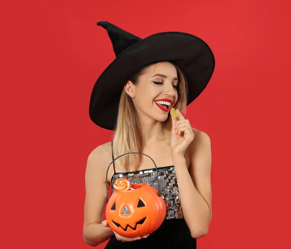 Hermosa mujer con traje de bruja con Jack O 'Lantern contenedor de caramelos sobre fondo rojo, espacio para el texto. Fiesta de Halloween — Foto de Stock
