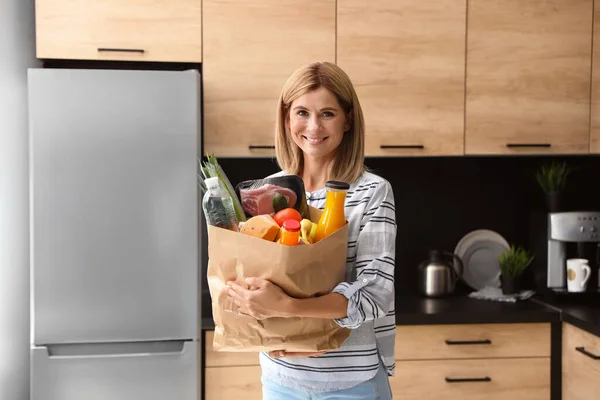 Nő papírzacskó tele termékek közelében hűtőszekrény a konyhában — Stock Fotó