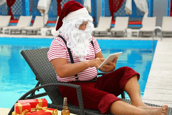 Tatil yerindeki şezlongda dinlenen tabletli otantik Noel Baba. — Stok fotoğraf