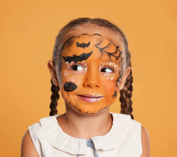 Menina bonito com pintura facial no fundo laranja — Fotografia de Stock