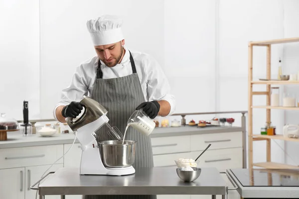 Male pastry chef preparing dough in mixer at kitchen table