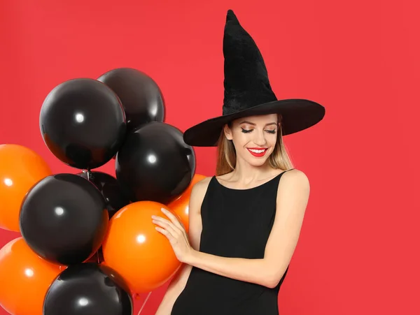 Mulher bonita vestindo traje de bruxa com balões para festa de Halloween no fundo vermelho — Fotografia de Stock