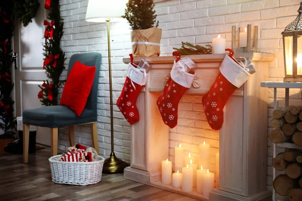 Red Christmas stockings with gifts on decorative fireplace in festive room interior — Stock Photo, Image
