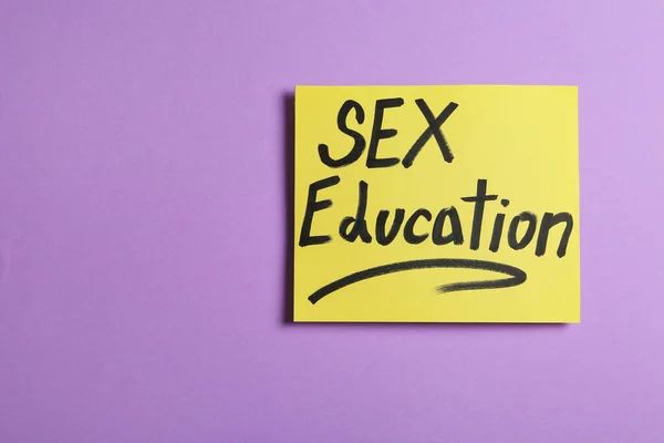 Nota con la frase "SEXO EDUCACIÓN" sobre fondo violeta, vista superior — Foto de Stock