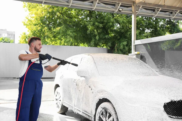 Jeune ouvrier nettoyage automobile avec jet d'eau haute pression au lavage de voiture — Photo