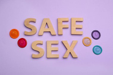 Düz kompozisyon, prezervatif ve kelimelerle. Menekşe arkaplanda ahşap harflerle yapılan güvenli seks.