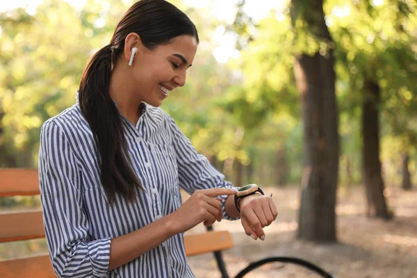 Mujer joven con auriculares inalámbricos y reloj inteligente en el parque — Foto de Stock