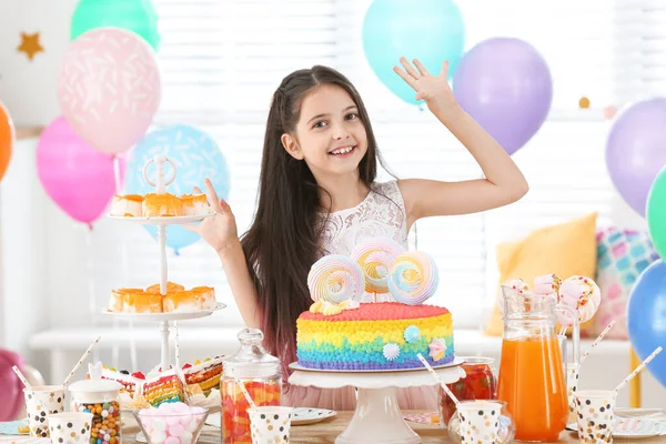 Masadaki mutlu kız, doğum günü partisi için dekore edilmiş odada ikramla. — Stok fotoğraf