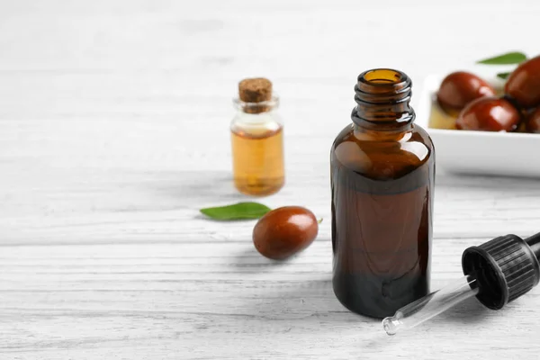 Glass bottle with jojoba oil and dropper on white wooden table. Space for text — Stock Photo, Image