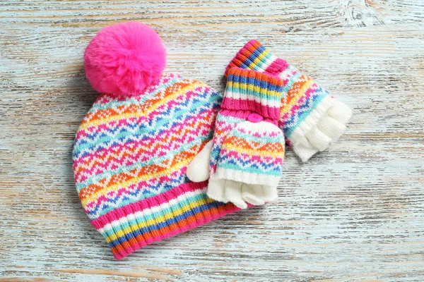 Warm knitted hat and mittens on wooden background, flat lay