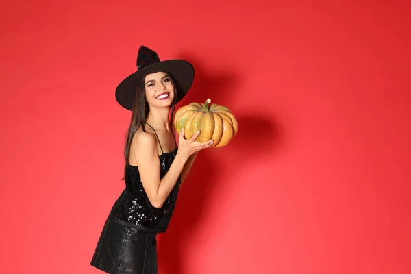Hermosa mujer joven con traje de bruja con calabaza para la fiesta de Halloween sobre fondo rojo, espacio para el texto —  Fotos de Stock