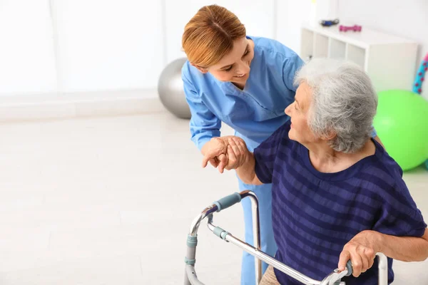 Správce pomáhající starší ženě s chodním rámečkem uvnitř — Stock fotografie