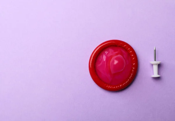 Red condom and pin on violet background, flat lay. Space for text — Stock Photo, Image