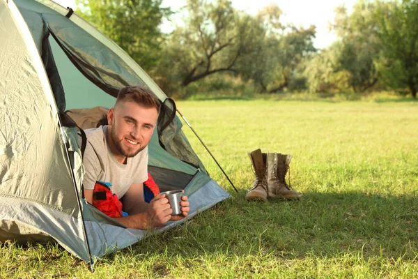 Jovem em saco de dormir com xícara de bebida deitado dentro da tenda de acampamento — Fotografia de Stock