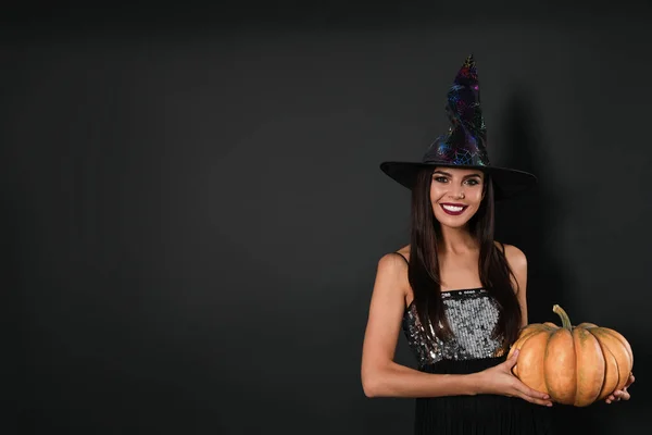 Hermosa mujer con traje de bruja con calabaza para la fiesta de Halloween sobre fondo negro, espacio para el texto —  Fotos de Stock