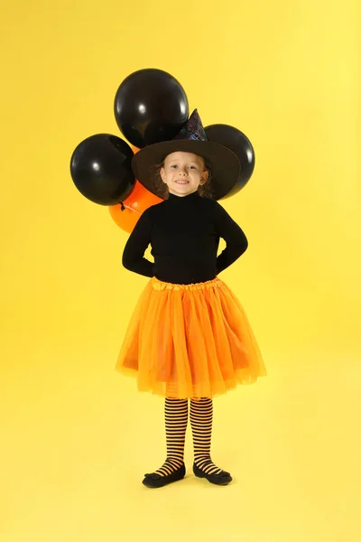 Söt liten flicka med ballonger bär Halloween kostym på gul bakgrund — Stockfoto