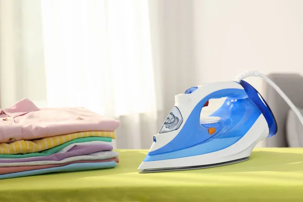 Brädan med modernt strykjärn och ren tvätt hemma — Stockfoto