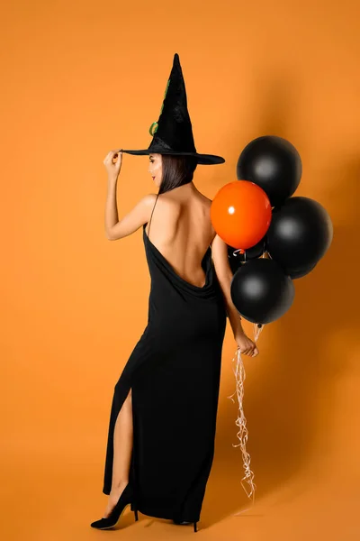 Bella donna che indossa costume da strega con palloncini per la festa di Halloween su sfondo giallo — Foto Stock