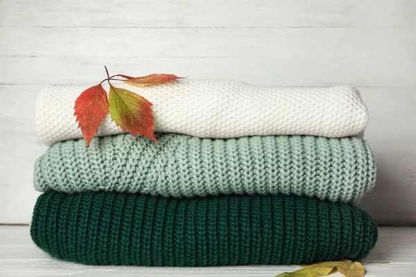 Stapel warme gebreide kleding en herfstbladeren op witte houten ondergrond — Stockfoto
