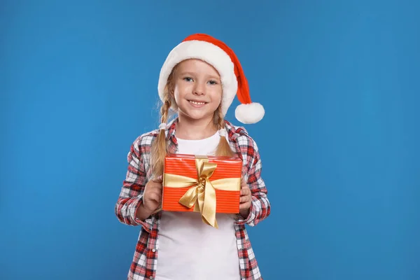 Criança feliz em chapéu de Papai Noel com caixa de presente em fundo azul. Celebração de Natal — Fotografia de Stock