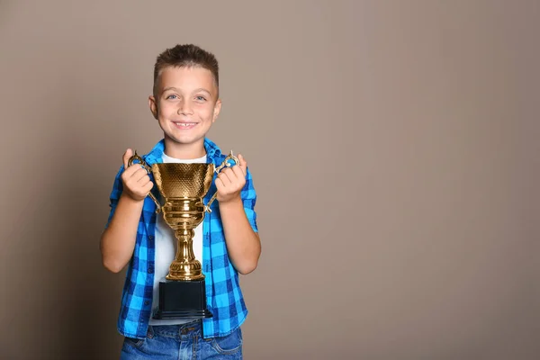Happy boy met gouden winnende beker op beige achtergrond. Ruimte voor tekst — Stockfoto