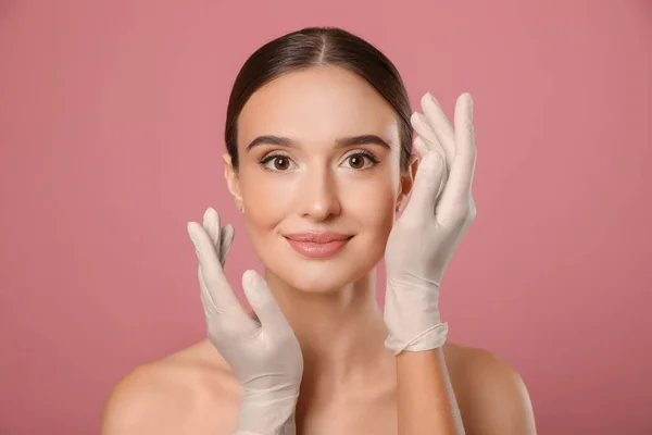 Médico examinando la cara de la mujer antes de la cirugía plástica sobre fondo rosa — Foto de Stock