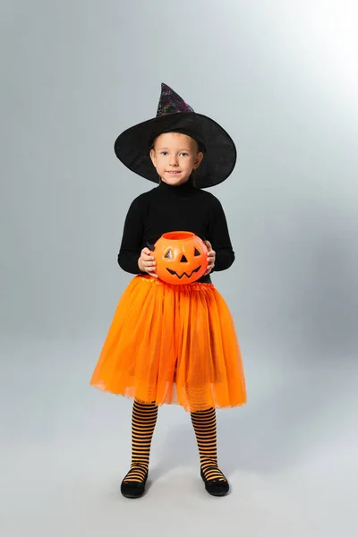 Menina bonito com abóbora doce balde vestindo traje de Halloween no fundo cinza — Fotografia de Stock