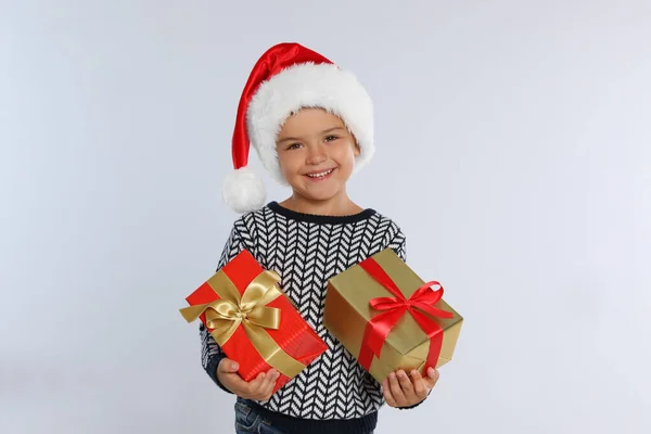 Щаслива маленька дитина в Санта-Каті з подарунковими коробками на світло-сірому фоні. Свято Різдва — стокове фото