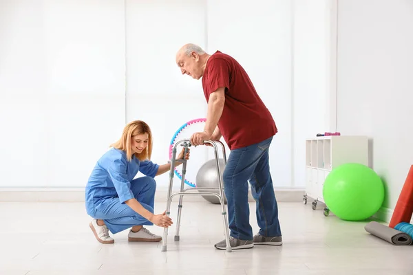Επιστάτης βοηθώντας τον ηλικιωμένο άνθρωπο με τα πόδια πλαίσιο σε εσωτερικούς χώρους — Φωτογραφία Αρχείου