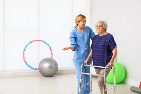 Cuidador ayudando a anciana con marco para caminar en interiores — Foto de Stock