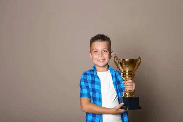 Happy boy met gouden winnende beker op beige achtergrond. Ruimte voor tekst — Stockfoto
