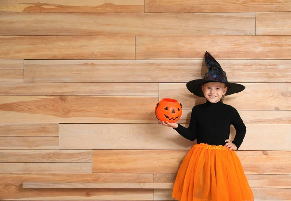 Jolie petite fille avec seau de bonbons à la citrouille portant un costume d'Halloween sur fond en bois. Espace pour le texte — Photo