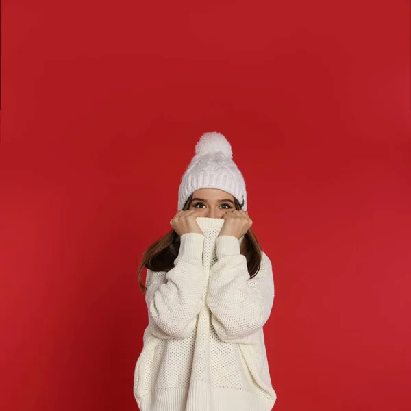 Belle jeune femme en pull blanc et chapeau sur fond rouge. Saison d'hiver — Photo