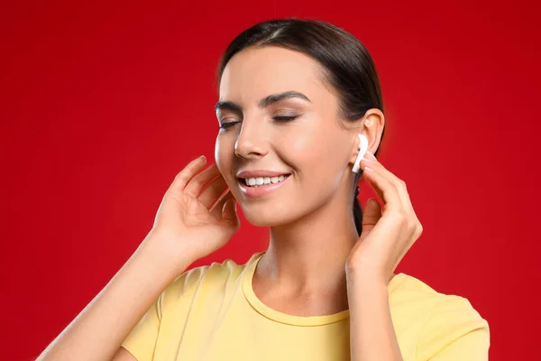 Χαρούμενη νεαρή γυναίκα ακούγοντας μουσική μέσω ασύρματων ακουστικών σε κόκκινο φόντο — Φωτογραφία Αρχείου