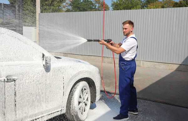 Young worker cleaning automobile with high pressure water jet at car wash