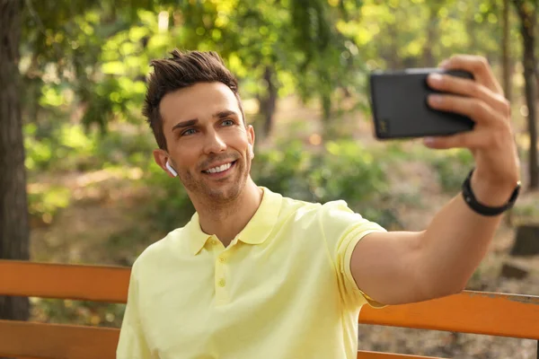 Jovem com fones de ouvido sem fio tirando selfie no parque — Fotografia de Stock