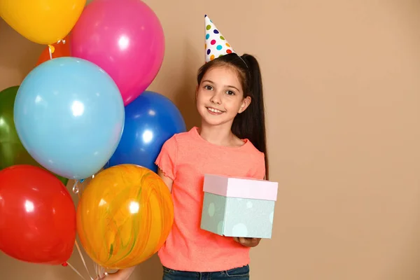 Mutlu kız, doğum günü hediyesi ve kahverengi arka planda balonlar. — Stok fotoğraf