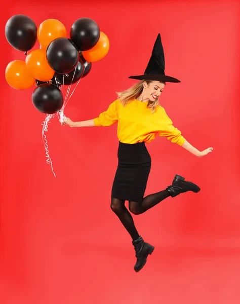 Schöne Frau trägt Hexenkostüm für Halloween-Party Springen mit Luftballons auf rotem Hintergrund — Stockfoto
