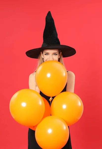Krásná žena na sobě čarodějnice kostým s balónky na Halloween party na červeném pozadí — Stock fotografie