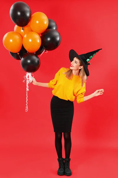 Beautiful woman wearing witch costume with balloons for Halloween party on red background — ストック写真