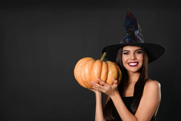 Beautiful woman wearing witch costume with pumpkin for Halloween party on black background, space for text — ストック写真