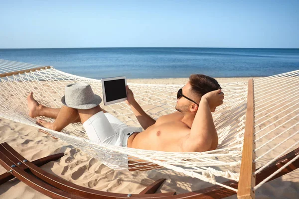 年轻人在海滩上的吊床上用平板电脑 — 图库照片