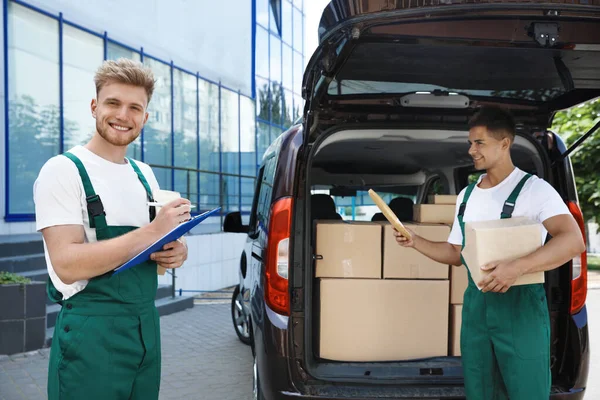 Correos jóvenes con paquetes cerca del coche de reparto al aire libre — Foto de Stock