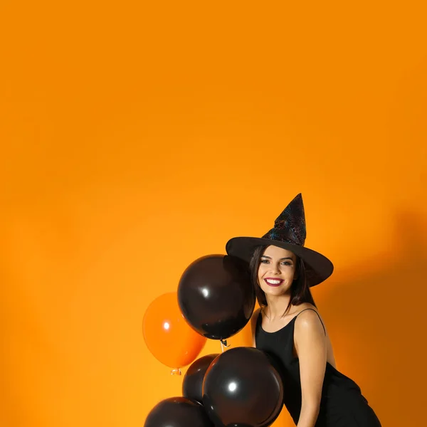 Mulher bonita vestindo traje de bruxa com balões para festa de Halloween em fundo amarelo, espaço para texto — Fotografia de Stock