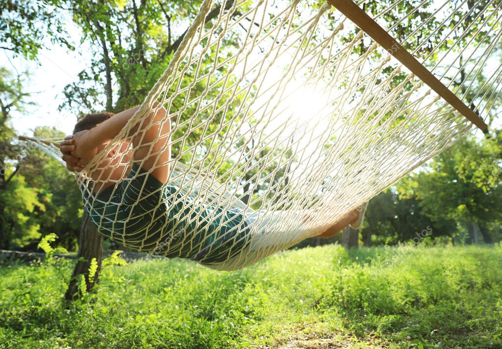 Young man resting in comfortable hammock at green garden