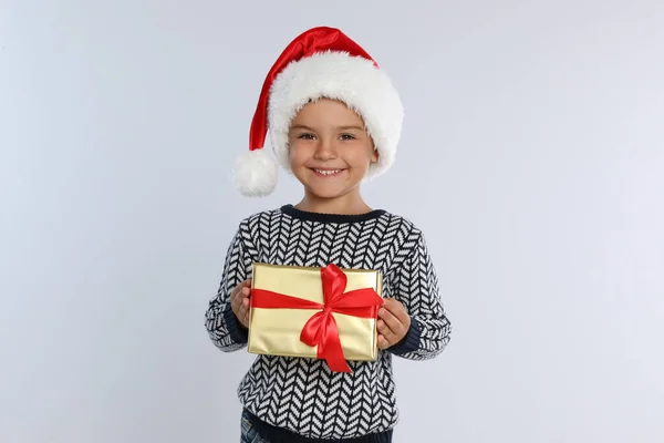 Criança feliz em chapéu de Papai Noel com caixa de presente em fundo cinza claro. Celebração de Natal — Fotografia de Stock
