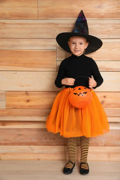 Schattig klein meisje met pompoen dragen Halloween kostuum in de buurt van houten muur — Stockfoto