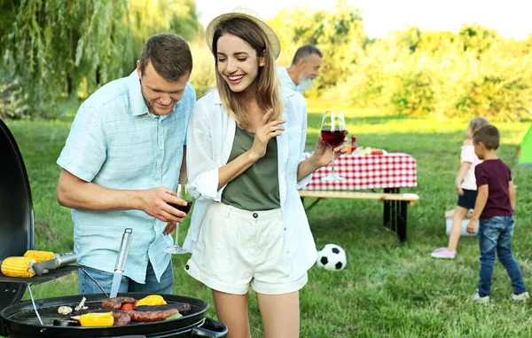 Família feliz fazendo churrasco no parque no dia ensolarado — Fotografia de Stock