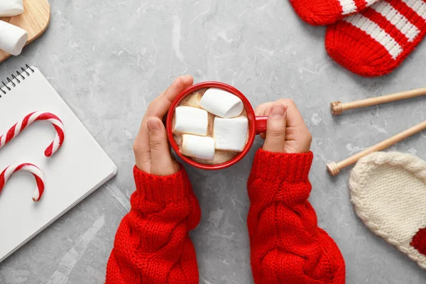 Frau hält Tasse mit leckerem Kakao mit Marshmallows am grauen Marmortisch, Draufsicht. gemütlicher Winter — Stockfoto