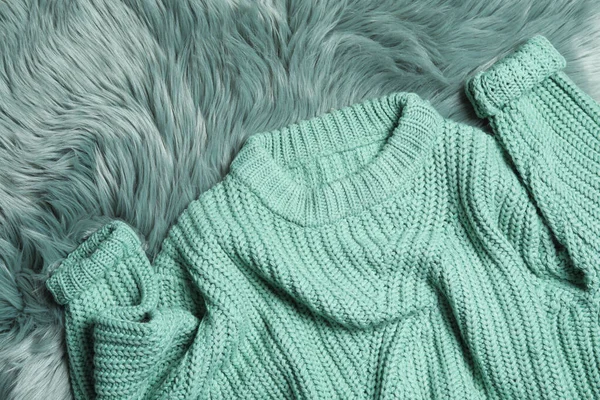 Soft knitted sweater on green fur rug, flat lay — Stock Photo, Image